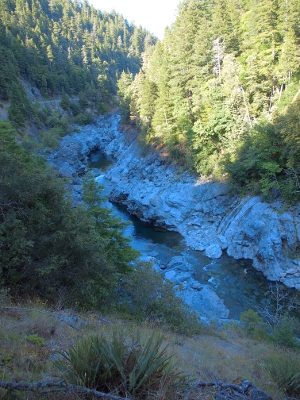 [A narrow river running through whitish-grey rocks in a valley. The setting sun puts all but the one tree'd hillside in shadow.]